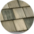 A circular image showing a close-up of a shingle roof with alternating gray and weathered wooden shingles. The texture and pattern of the shingles are clearly visible.