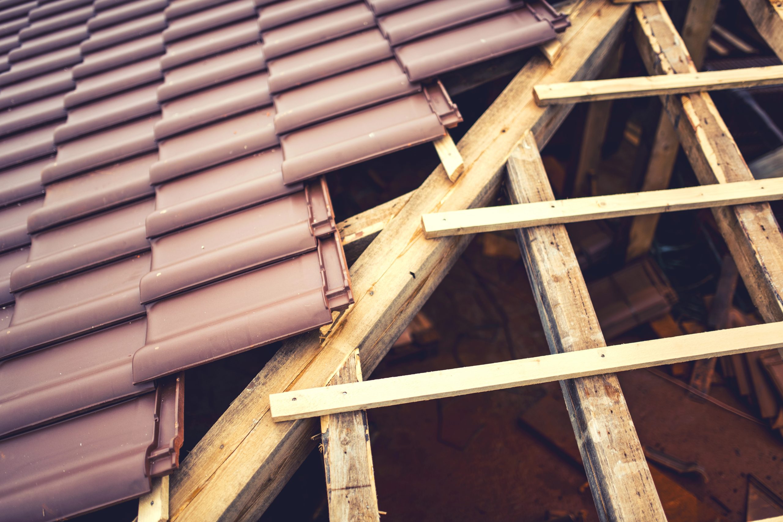 Partially constructed roof with reddish-brown tiles aligned on the left side, while the right side reveals exposed wooden beams and framework. The contrast highlights the ongoing installation of sustainable roofing materials designed for weather resistance.