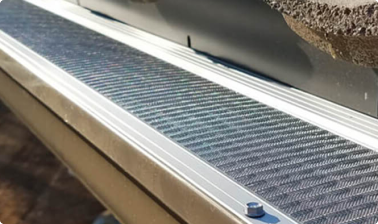Close-up of a metal gutter guard installed along the edge of a roof, designed to prevent debris from entering the gutter while allowing water to pass through.
