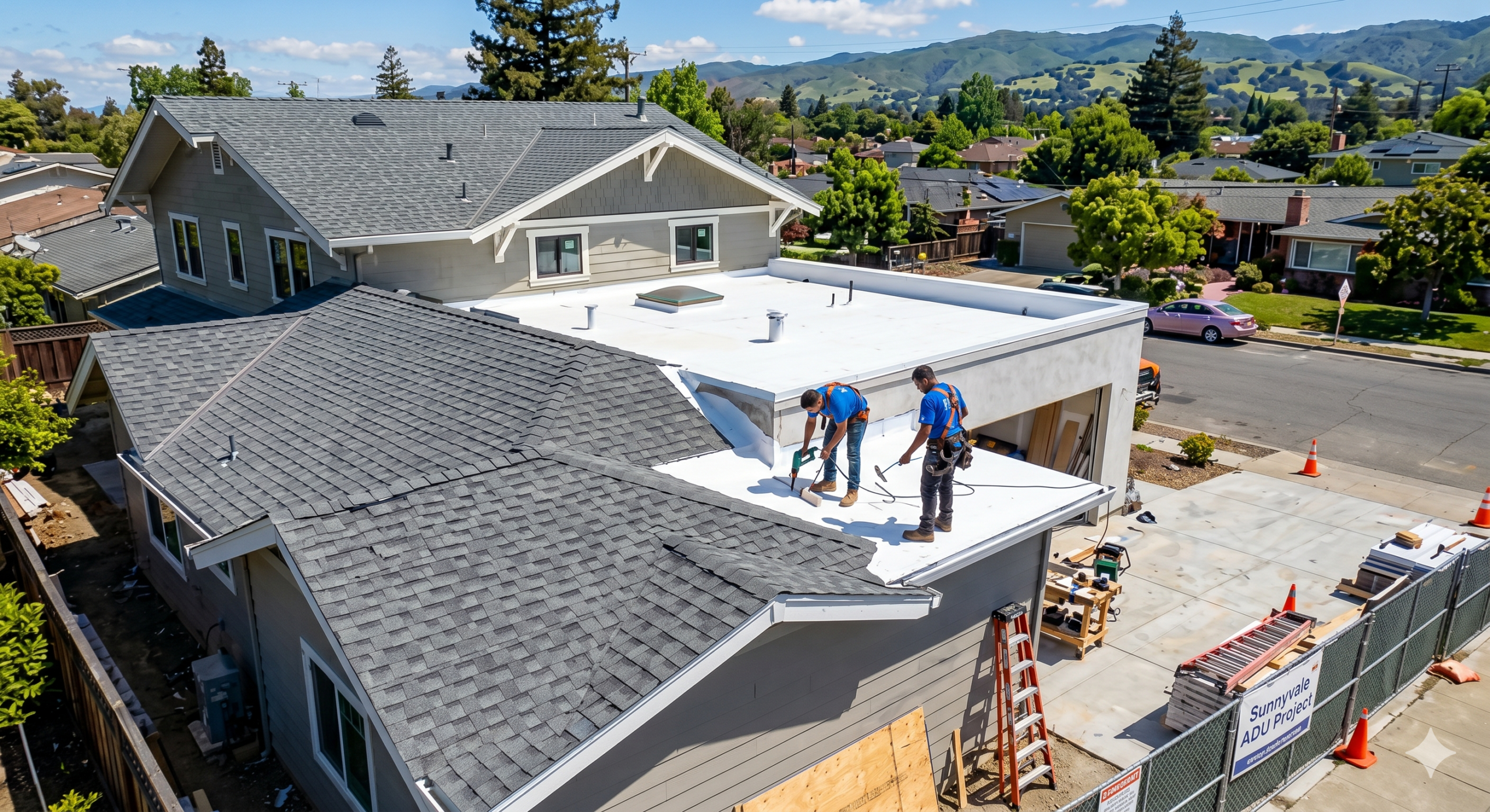 Two workers wearing safety harnesses install roofing material on a flat roof in a suburban neighborhood, with houses, trees, and hills in the background. Perfect for home additions or Sunnyvale ADU projects on a sunny day.